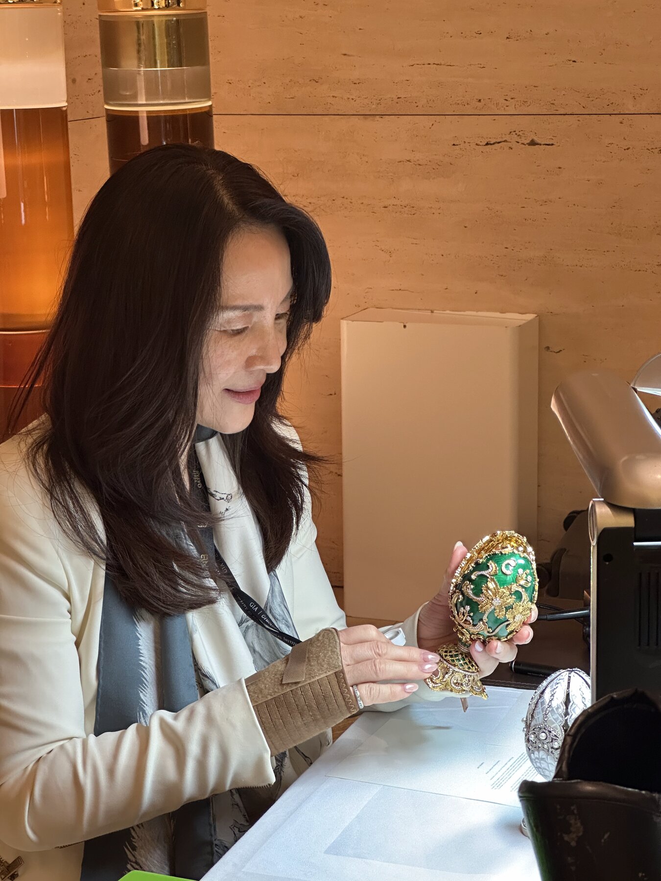 Kehan Li holding a green and gold Faberg&eacute; egg in her hands, examining it attentively.